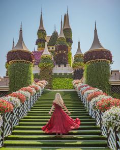 a woman in a red dress is walking down some stairs with flowers on the side