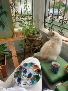 a white cat sitting on top of a green cushion next to a painting easel