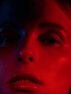 a woman's face with red and blue light shining on her cheek, close up