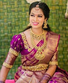 a woman in a purple and gold sari sitting on a red couch with green wallpaper behind her