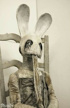 a statue of a rabbit sitting in a chair with its head covered by yarn and hair