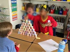 two children are playing with a pyramid made out of cans and paper cups on the table