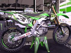 a green and white dirt bike sitting on top of a stand in front of a truck