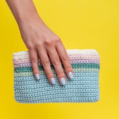 a woman's hand on top of a crocheted purse with white nails