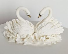 two white swans sitting on top of each other in the shape of flowers and leaves