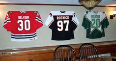 three hockey jerseys are hanging on the wall in a restaurant with wooden tables and chairs