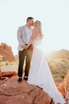 a bride and groom kissing on top of a rock formation in the desert at sunset