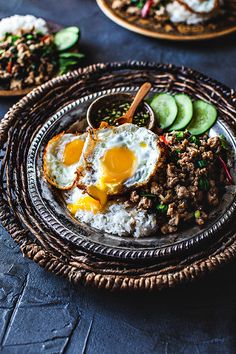 two plates filled with rice, meat and fried eggs on top of cucumbers