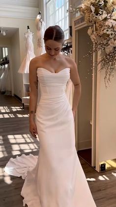 a woman in a white wedding dress looking down at the floor with her hand on her hip