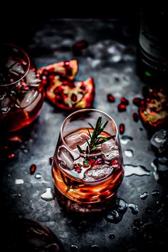 two glasses filled with drinks sitting on top of a metal table next to some pomegranates