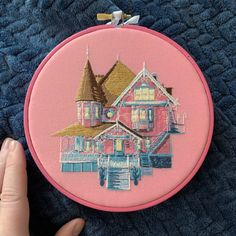 a hand is holding up a pink embroidery hoop with a house on the front and side