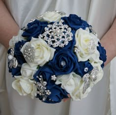 a bridal bouquet in blue and white with brooches on the bride's arm