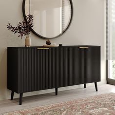 a black cabinet with gold handles in front of a round mirror and rug on the floor