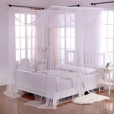 a white bed sitting on top of a hard wood floor next to two large windows