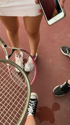 two people standing next to each other holding tennis racquets and cell phones