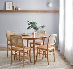 a dining room table with four chairs and a potted plant in the corner on top of it