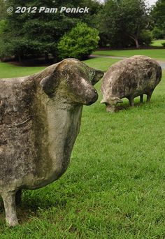 two stone cows standing on top of a lush green field