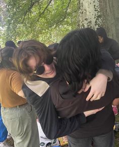 two girls hugging each other in front of a group of people under a tree with their arms around one another