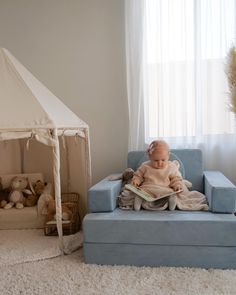 a baby sitting on a blue chair in front of a window with a white tent