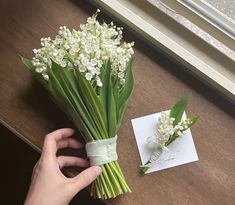 a person is holding some flowers on a table next to a card and window sill