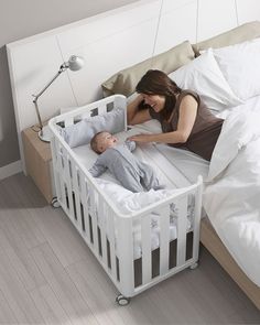 a woman laying in bed next to a baby sleeping inside of a white crib