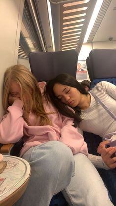 two women are sleeping on a train next to each other and one is holding a cell phone