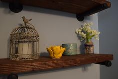 a bird cage sitting on top of a wooden shelf next to vases and flowers