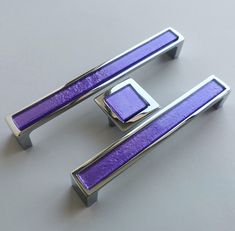 two purple and silver metal handles on a gray surface, one has a square shaped handle