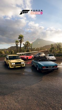 four cars are parked in a parking lot with mountains in the background and clouds in the sky