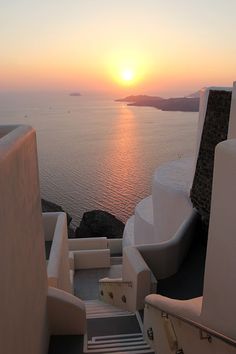 the sun is setting over an ocean with white buildings