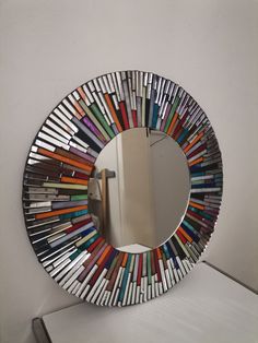 a round mirror with multicolored sticks sticking out of it's sides on a white wall