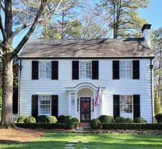 a white house with black shutters and a flag on the front door is shown