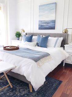 a bed with blue and white pillows in a bedroom next to a painting on the wall