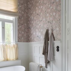 a white bath tub sitting next to a window in a bathroom with pink wallpaper