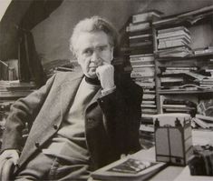 an old photo of a man sitting at a desk in front of a bookshelf