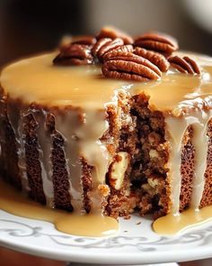 a cake with frosting and pecans on top sitting on a white platter