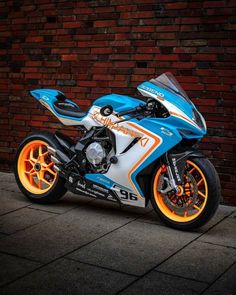 a blue and white motorcycle parked in front of a brick wall with orange rims