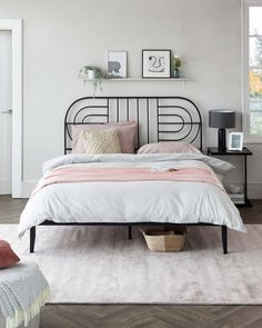 a bedroom with white walls and wood flooring has a black metal bed frame, pink sheets, and pillows