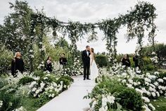 a bride and groom standing in front of an archway with white flowers at their wedding