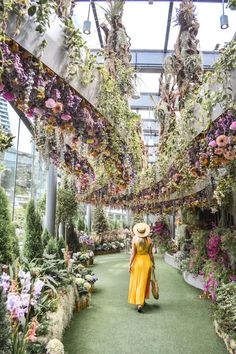 a woman in yellow dress and straw hat walking down a walkway with lots of plants