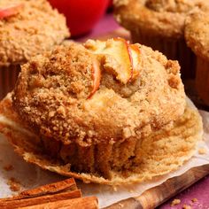 some muffins with apples in the background and cinnamon sticks next to them on a piece of paper