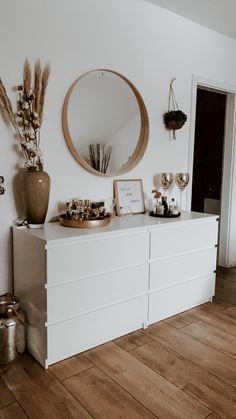 a white dresser sitting in front of a mirror on top of a wooden floor next to a vase