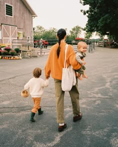 a woman walking with two small children on her back and an adult holding the child's hand