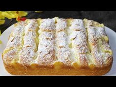 a white plate topped with a cake covered in powdered sugar next to yellow flowers