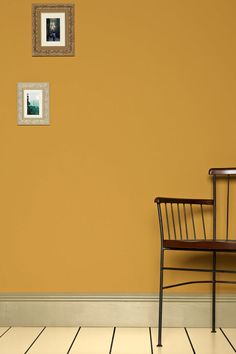 an empty chair sits in front of a wall with two pictures on it and a table next to it