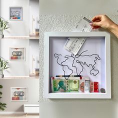 a hand holding a piece of paper in front of a shadow box with money on it