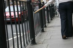 a woman is walking down the sidewalk with a stick in her hand and she's holding onto a fence