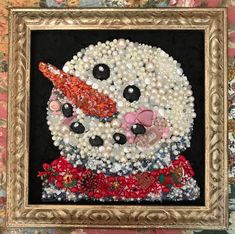 a snowman made out of buttons and pearls in a gold frame on a wall