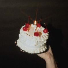 a hand holding a cake with candles and cherries on it