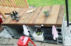 an outdoor table made out of pallets with bottles and cans on it, next to a red chair